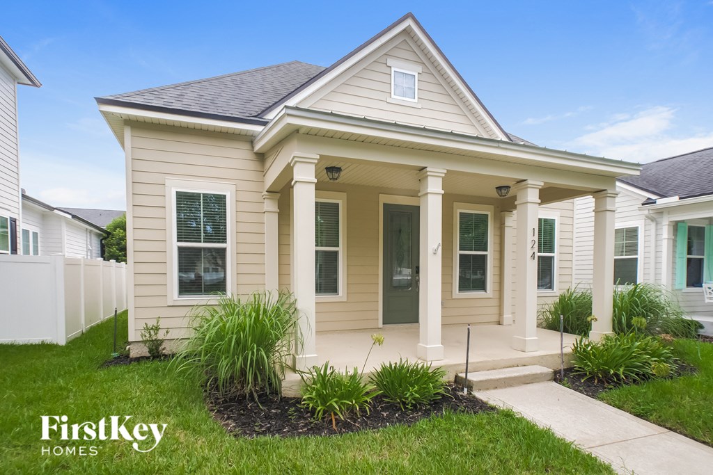a beige house with white pillars and a sidewalk