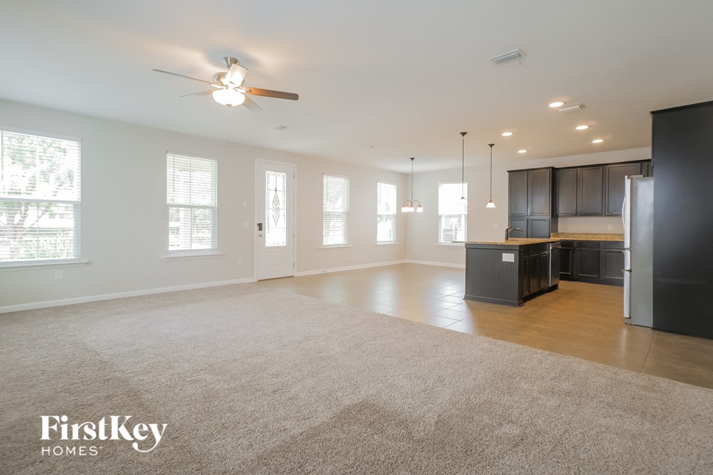 an empty living room with a kitchen and a ceiling fan