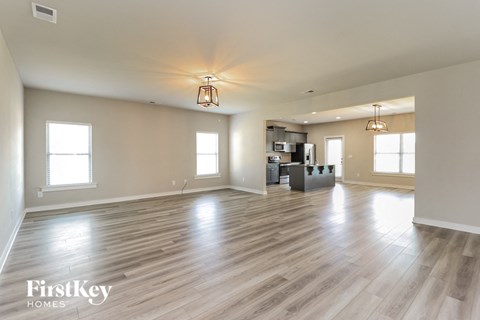 A spacious room with wooden floors and a kitchen area in the background.