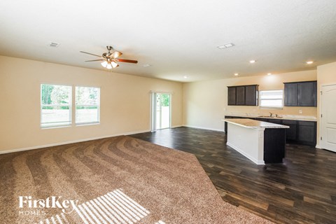 A spacious living room with a rug on the floor and a kitchen area in the background.