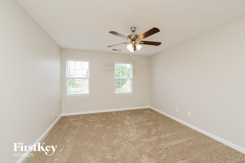 an empty room with a ceiling fan and two windows