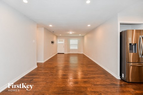 A long hallway with wood floors and a stainless steel refrigerator on the right.