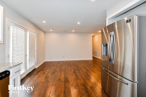 A stainless steel refrigerator sits in a kitchen with wooden floors and white walls.