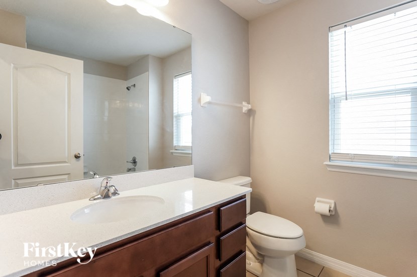 A bathroom with a toilet, sink, mirror, and window.