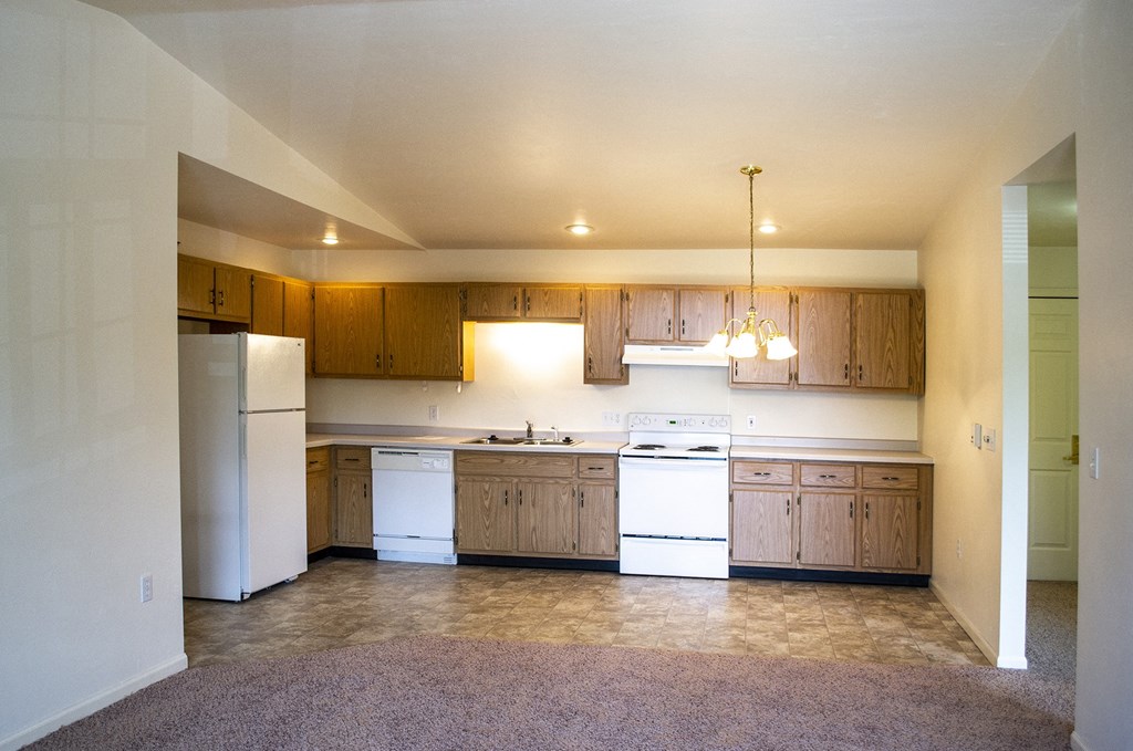 an empty kitchen with white appliances and wooden cabinets