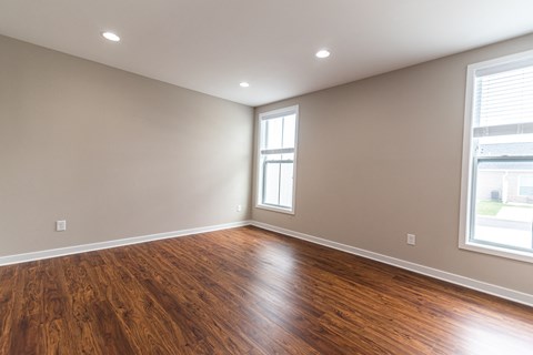 an empty living room with wood flooring and two windows
