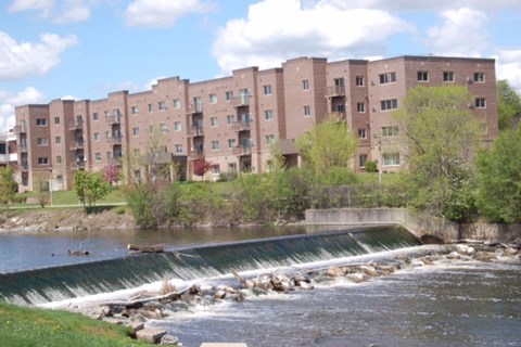 A river flows past a dam and apartment buildings.