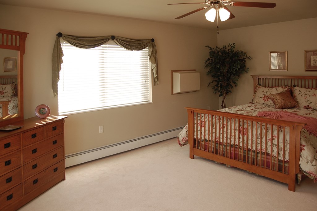 A baby's room with a crib, dresser, and a ceiling fan.