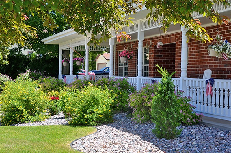 a red brick house with a white porch and landscaped front yard