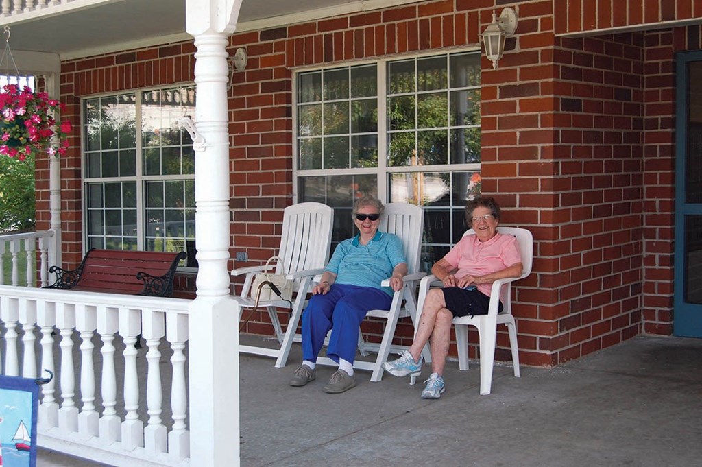 two women sitting in rocking chairs outside of a house