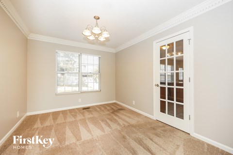 A room with a carpet floor, a door, a window, and a chandelier.