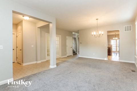 A spacious living room with a grey carpet and a chandelier.