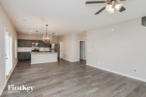 A spacious living room with a kitchen in the background and a ceiling fan above.