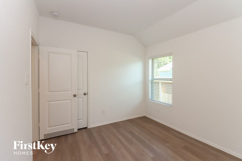 a bedroom with white walls and wood floors and a window