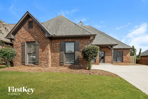 A brick house with a black window and a small tree in front.
