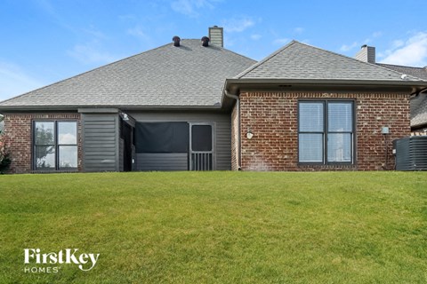 A house with a grey roof and a brick wall is shown with a grassy lawn in front.