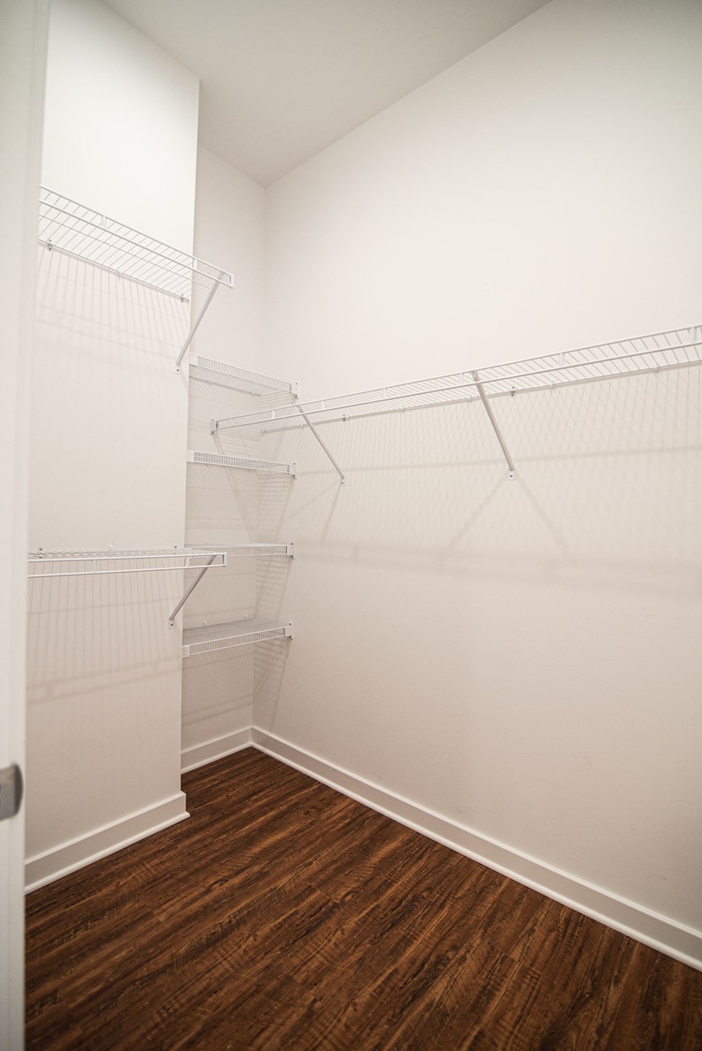 a room with white walls and a wood floor and a closet with white shelves