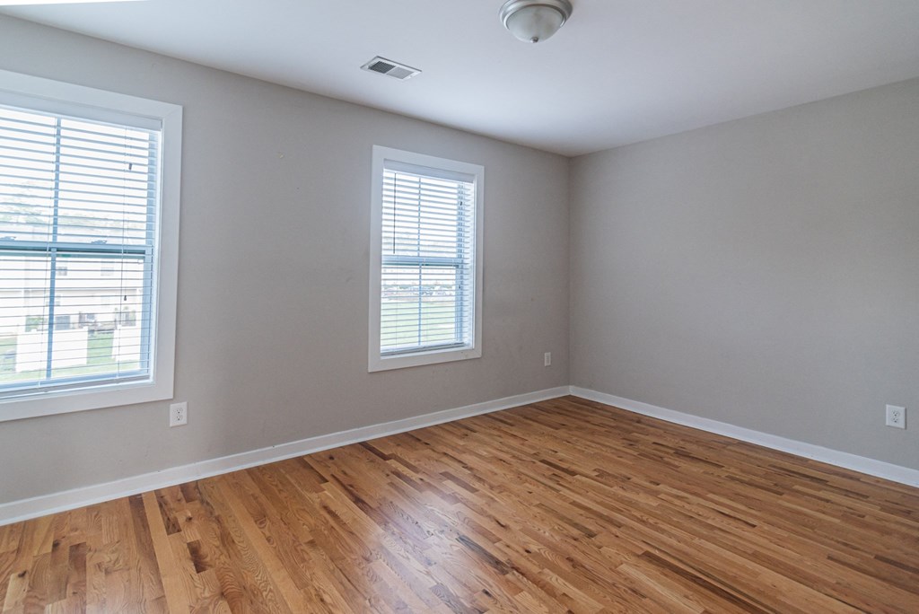 an empty room with wooden floors and two windows