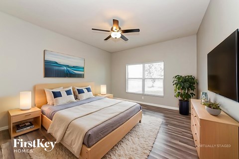 A bedroom with a bed, a ceiling fan, a painting, a potted plant, and a TV.
