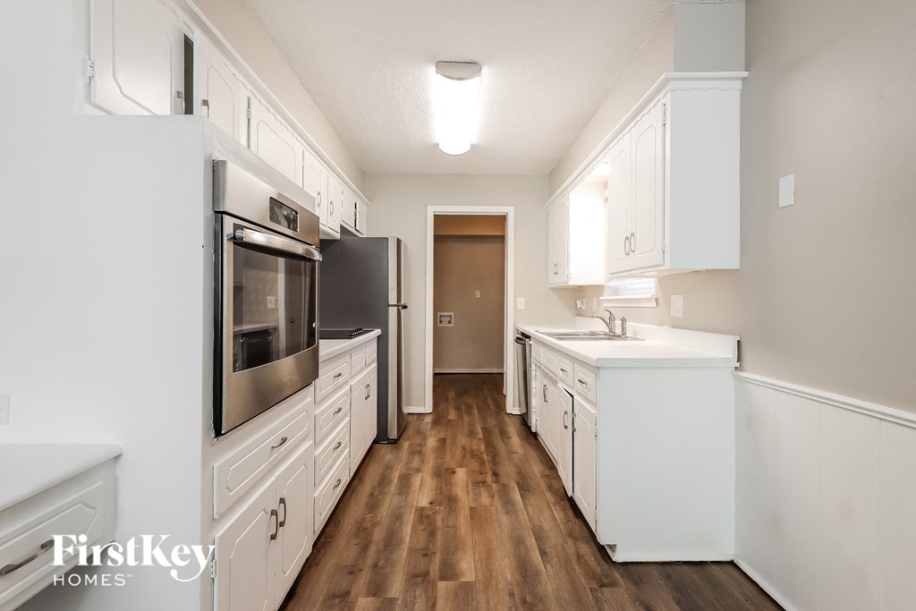 a kitchen with white cabinets and wood flooring and white appliances