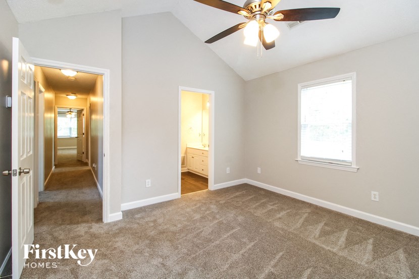 an empty living room with a ceiling fan and a hallway to a bedroom