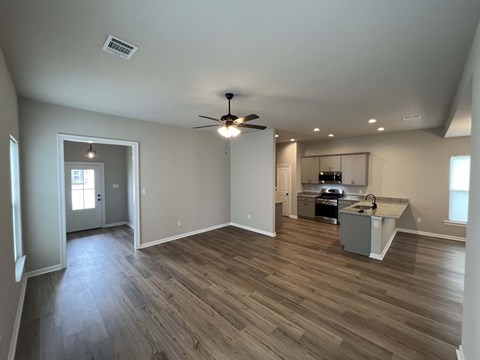 an empty living room with a kitchen and a ceiling fan