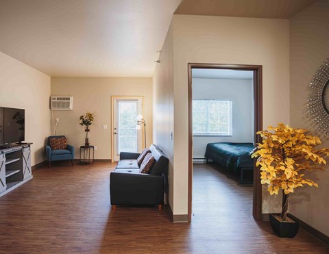 A living room with a black couch and a wooden floor.
