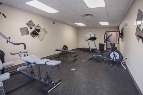 A gym room with a variety of equipment including a rowing machine, a leg press machine, and a bench press.