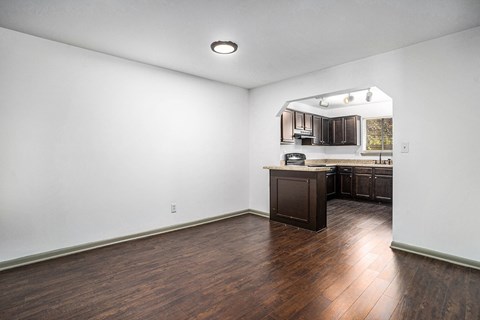 an empty living room and kitchen with wood floors and white walls