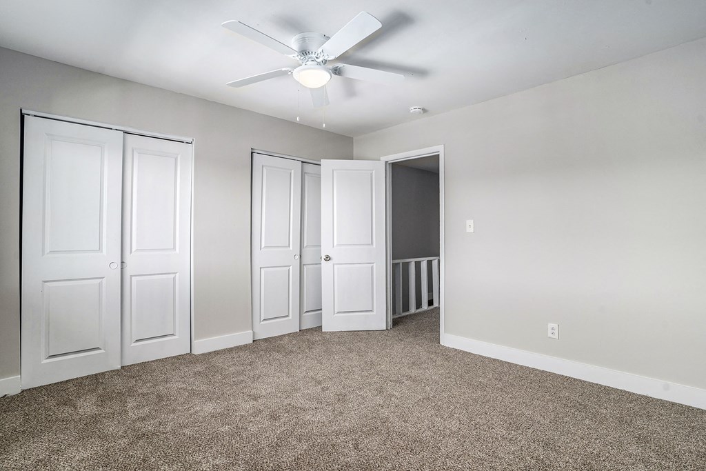 an empty bedroom with white doors and a ceiling fan