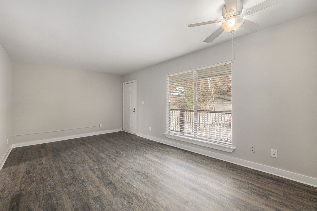 an empty living room with a large window and a ceiling fan