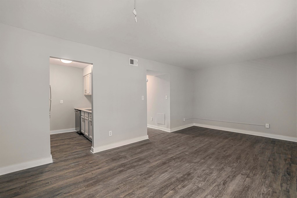 an empty living room with wood flooring and a kitchen