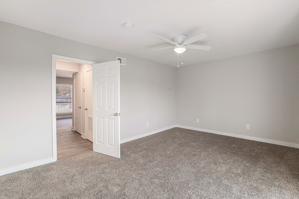 an empty living room with a ceiling fan and a door to a bedroom