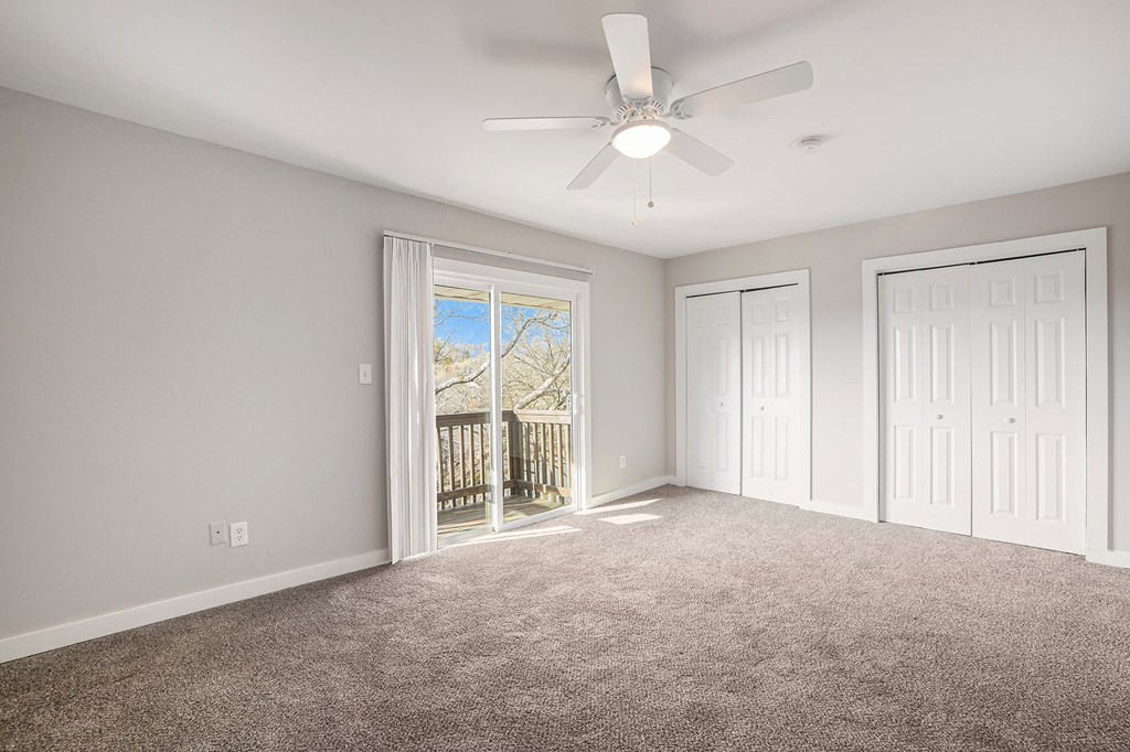 an empty living room with a ceiling fan and a balcony