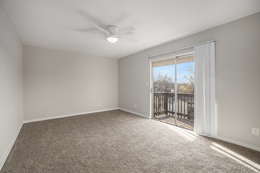 an empty living room with a large window and a ceiling fan