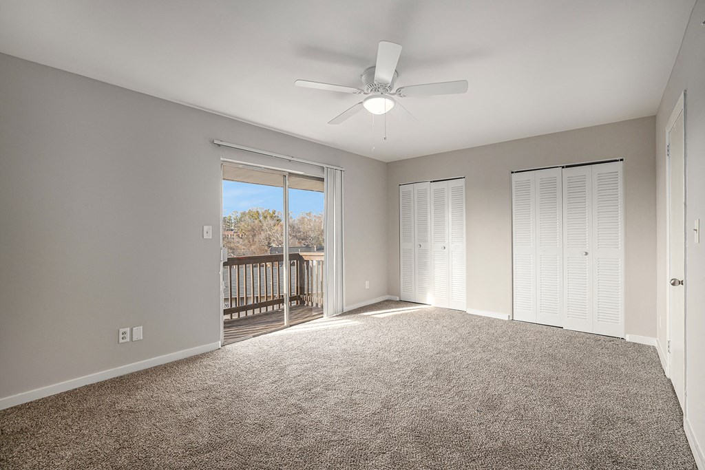 an empty living room with a ceiling fan and a balcony
