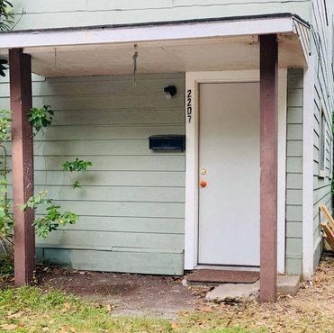 A white door is on the right side of a small building with a porch.