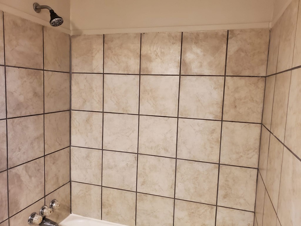 A shower with a beige tile wall.