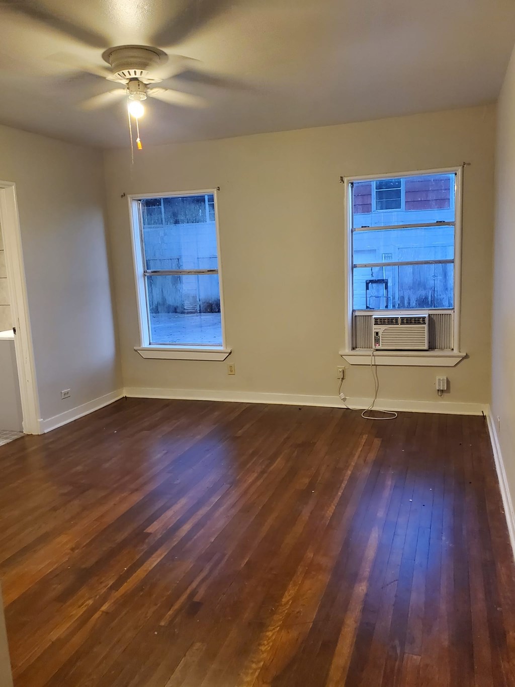 A room with a ceiling fan and two windows.