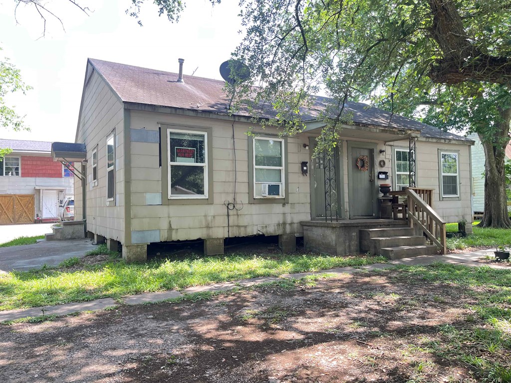 A small, old house with a porch and a tree in front.