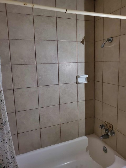 A white bathtub with a shower head and a toilet paper holder on the wall.