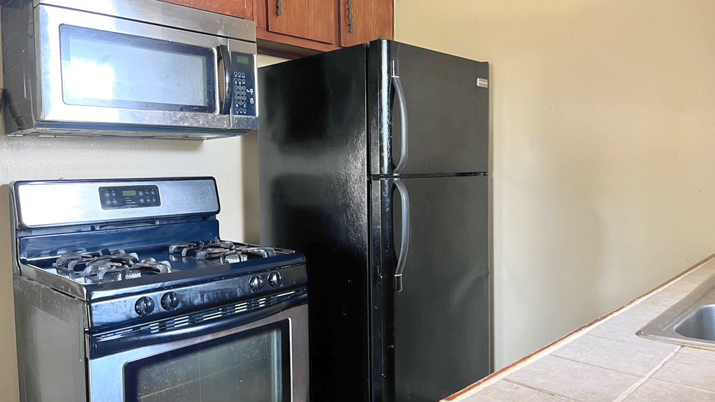 A black refrigerator stands next to a stove in a kitchen.