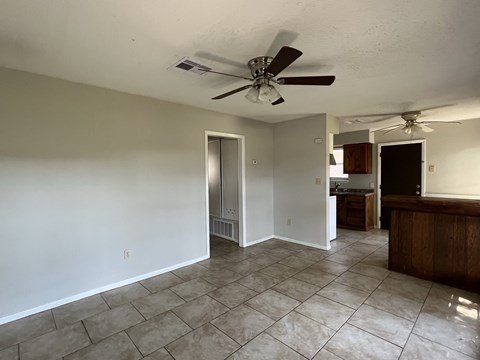 an empty living room with a ceiling fan and a kitchen