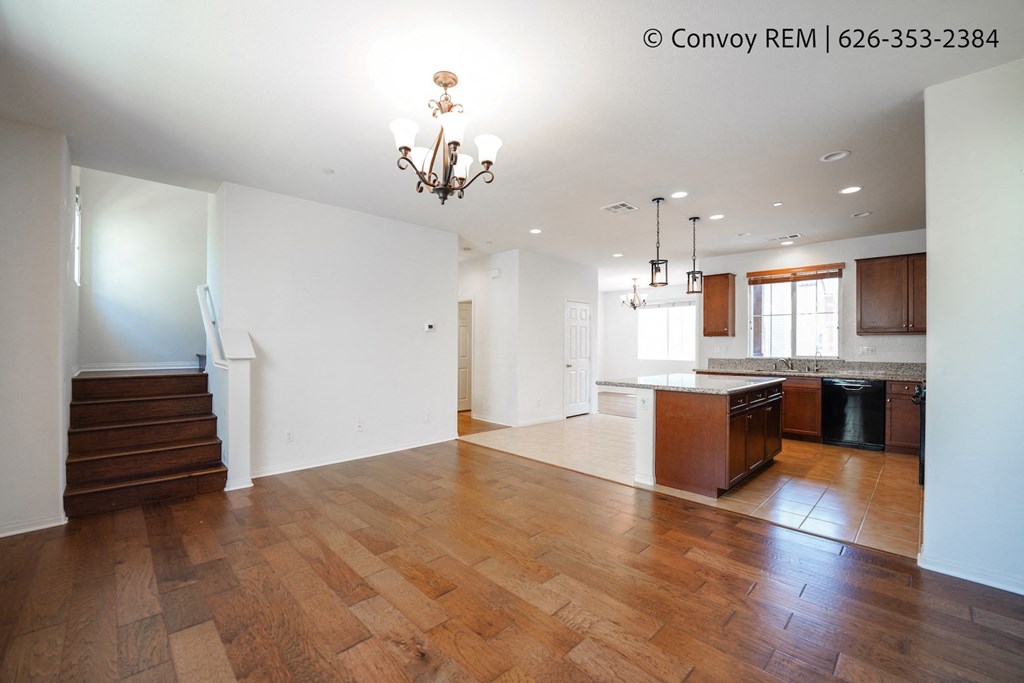an empty living room and kitchen with wood flooring and a chandelier