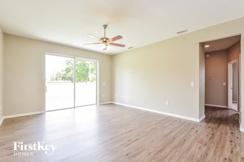 A spacious room with a ceiling fan and sliding glass doors leading to a balcony.
