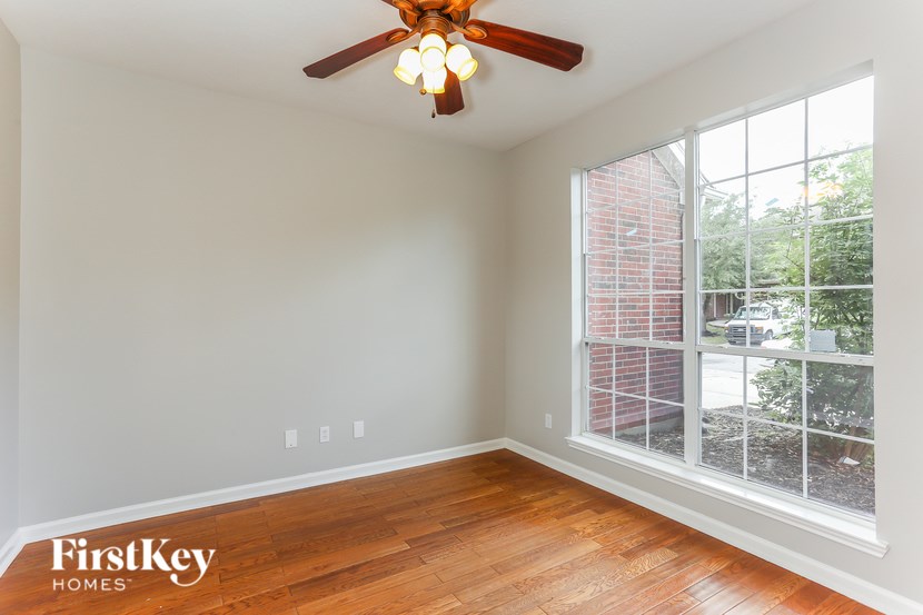 A room with a ceiling fan and a window overlooking a brick building.
