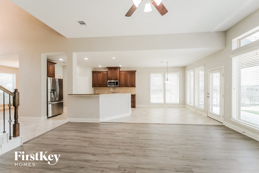 an empty living room with a kitchen and a ceiling fan