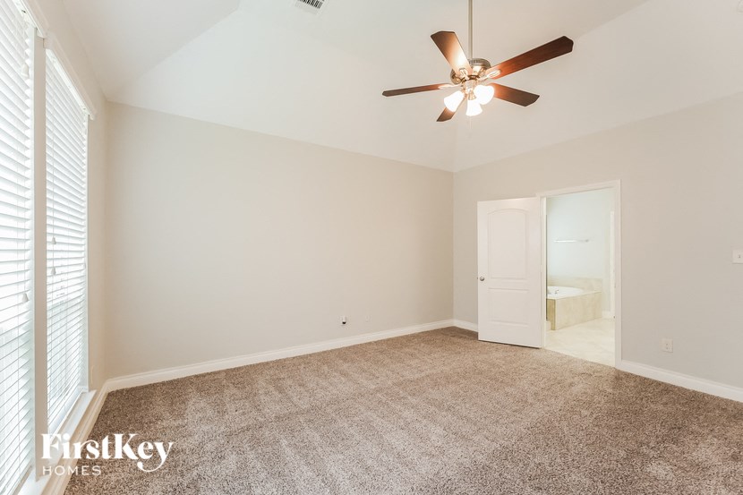 an empty living room with a ceiling fan and a door to a bathroom