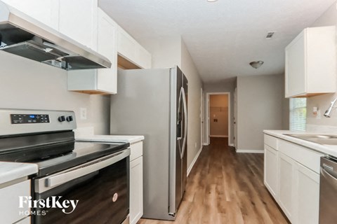 A kitchen with a stove top oven, refrigerator, and wooden floors.