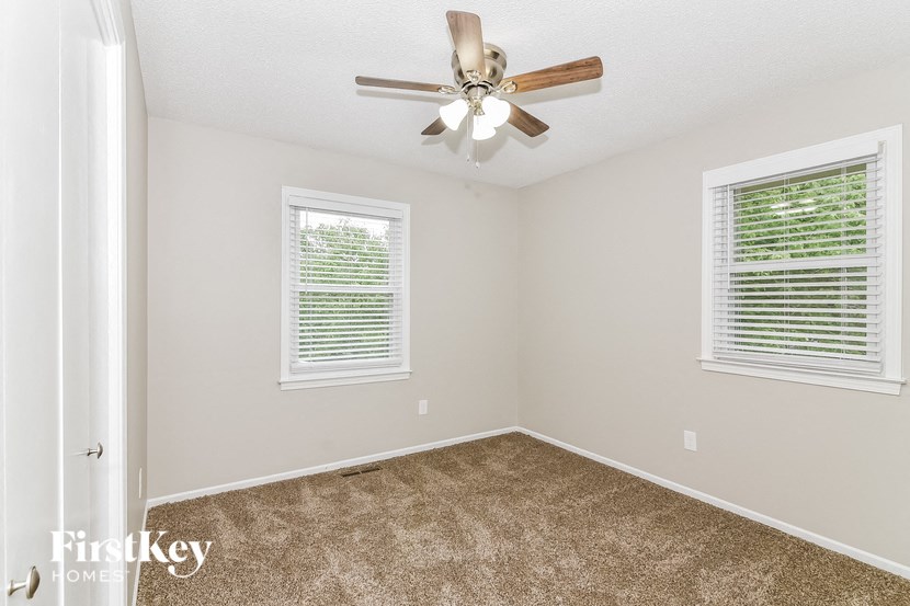 an empty bedroom with a ceiling fan and two windows